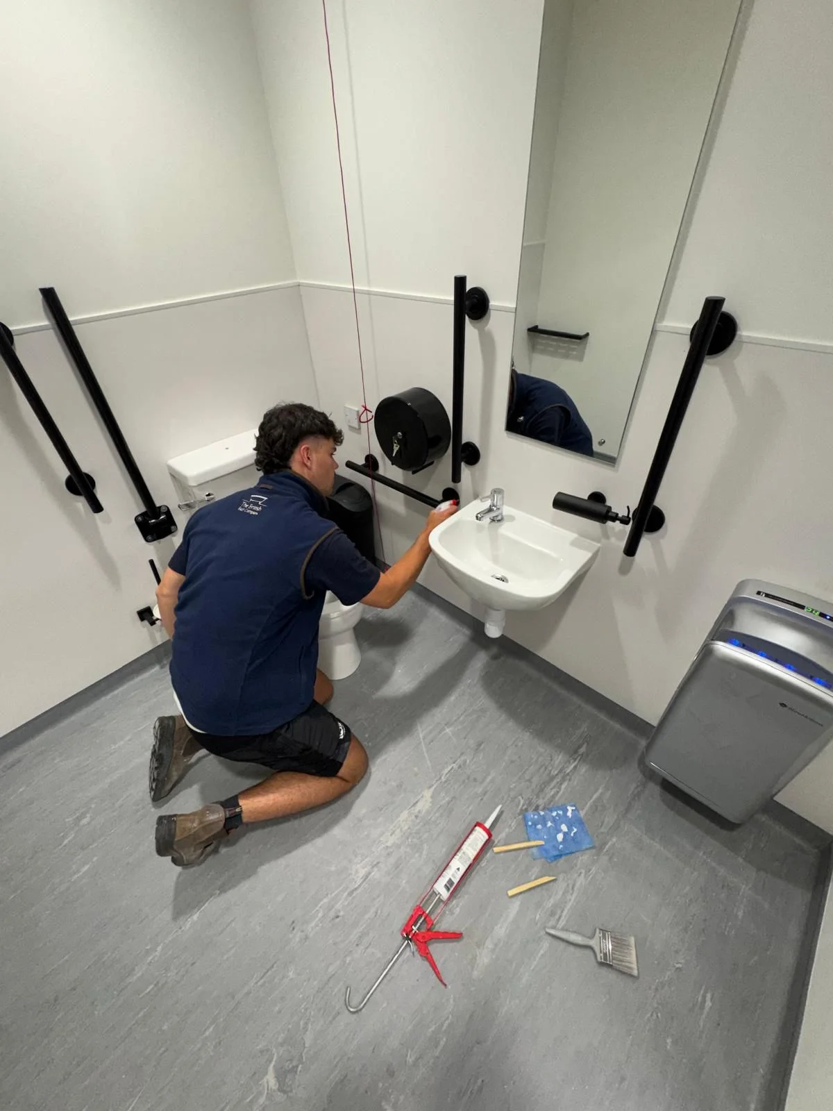 A team member finishing sealant around a basin in an accessible bathroom